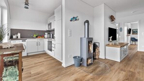 Moderni keittiö, jossa on valkoiset kaapit, sisäänrakennettu liesi sekä ruokailutila, jossa on puinen pöytä ja sininen tuoli.
