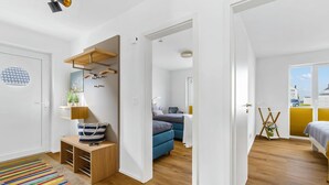 A modern, well-lit room with a wooden floor, a colorful striped rug, a bed with a white headboard, a blue sofa, and a small wooden table with a lamp. - 2 bedroom beach front home in Olpenitz (Olpenitz)