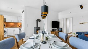A modern, well-lit living room with a dining area set for a meal, a kitchen with white cabinets, and a fireplace. - 2 bedroom beach front home in Olpenitz (Olpenitz)