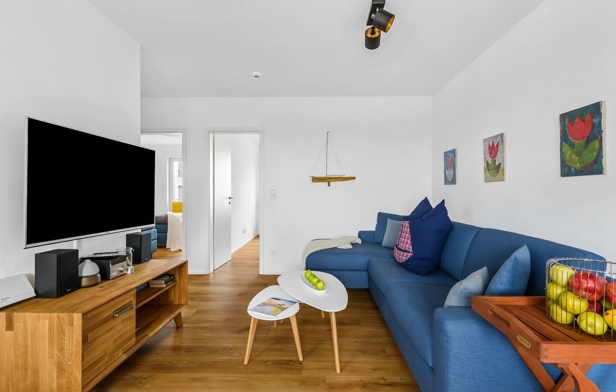 A modern living room with a flat-screen TV, wooden furniture, a blue sofa, and artwork on the walls.