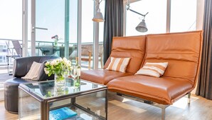 Ein modernes Wohnzimmer mit Ledersofa, Glastisch und Blick auf die Stadt durch große Fenster.