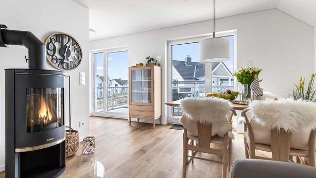 Een moderne woonkamer met een zwart houthaard, houten meubels en uitzicht op huizen door grote ramen.