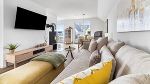 Een moderne woonkamer met een flatscreen televisie, een open haard, een bank en een eethoek met uitzicht op gebouwen.
