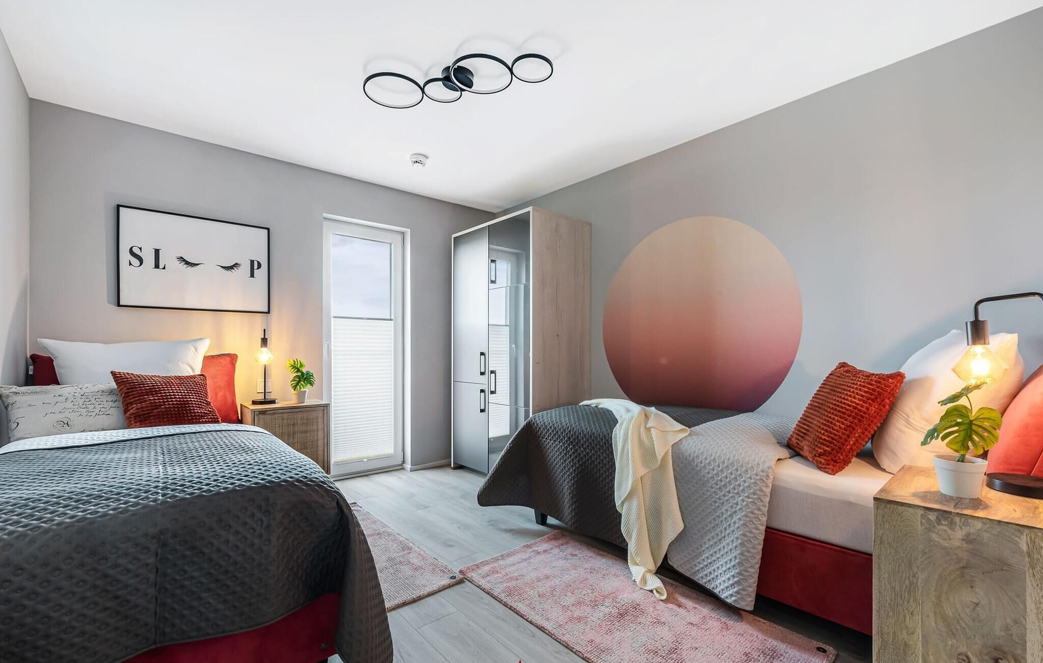 Un dormitorio moderno con dos camas, un adorno circular grande en la pared y una lámpara en el techo.
