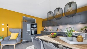 Una cocina moderna con zona de comedor, que presenta un sofá gris, una mesa de comedor de madera y una pared de acento amarilla.