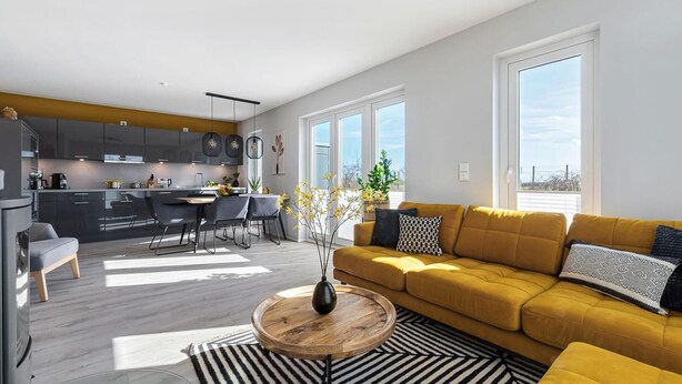 Una sala de estar moderna con un sofá amarillo, una zona de comedor y una cocina con armarios grises.