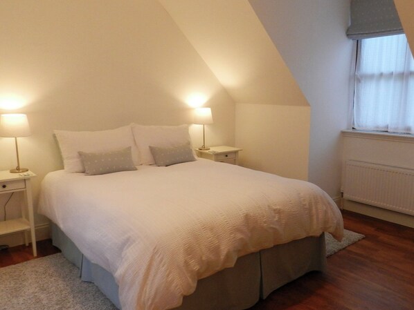 A bedroom with a large bed, two bedside tables, and a window with curtains.