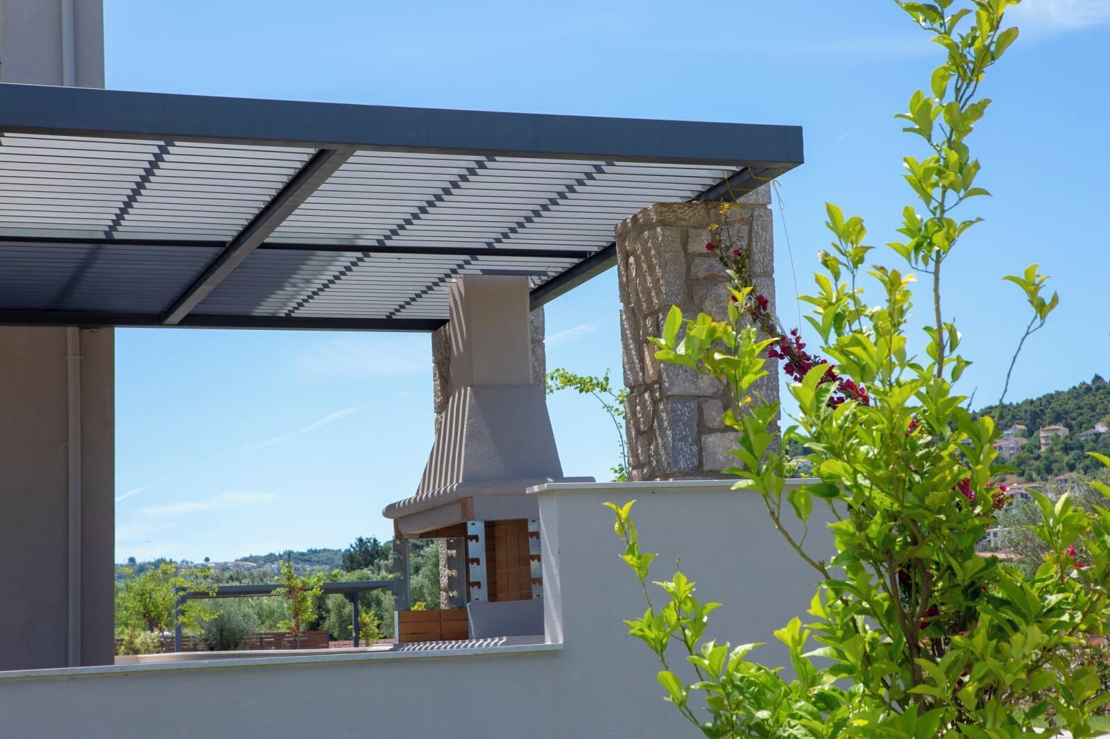 Un bâtiment moderne doté d’un toit en pente, d’une cheminée en pierre et offrant une vue sur un paysage vallonné.