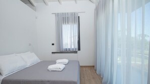 Un dormitorio moderno con cama, ventana con cortinas translúcidas y vistas al exterior.