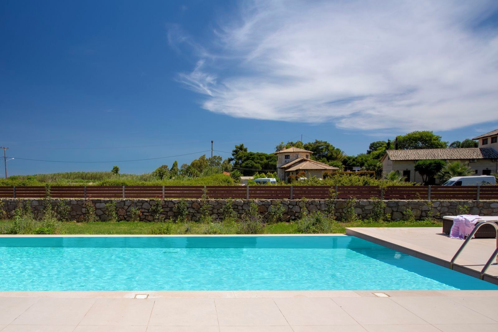 Piscina com muro de pedra e céu azul límpido.