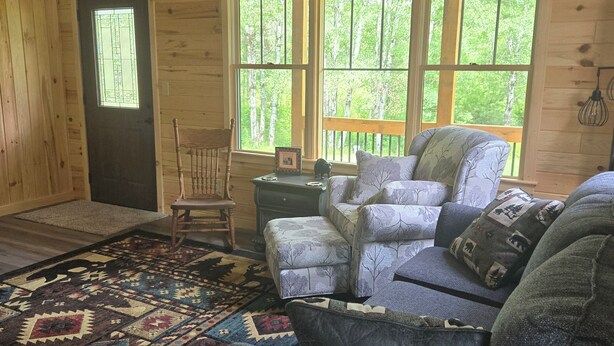 A cozy cabin interior with a large window, a patterned rug, and a blue sofa. - Right on the Tuscobia Trail Cozy 2-bedroom cabin in  Winter with WiFi,  AC  (Winter)