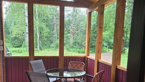 A covered outdoor seating area with a round table and four chairs, surrounded by wooden beams and red paneling. - Right on the Tuscobia Trail Cozy 2-bedroom cabin in  Winter with WiFi,  AC  (Winter)