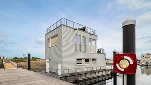 Ein kleines, einstöckiges Gebäude mit flachem Dach und Balkon in der Nähe eines Gewässers.