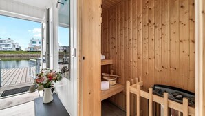Eine Holzhütte als Sauna mit einer Holzbank, einem Handtuchregal und einem Fenster mit Blick auf ein Gewässer.