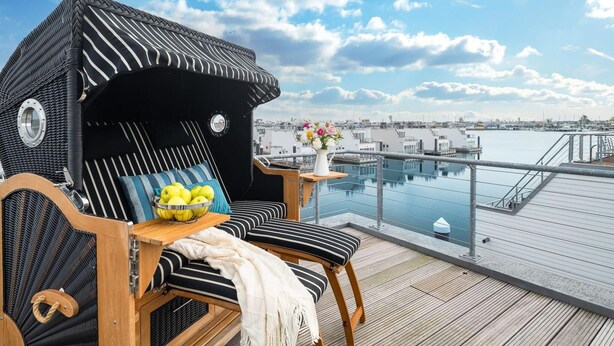 Ein Balkon mit einem gestreiften Stuhl, einem kleinen Tisch mit Blumenvase und Blick auf den Hafen.