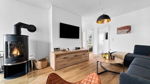 A modern living room with a wood-burning stove, a sofa, a TV, and a dining area.