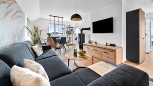 A modern living room with a grey sofa, a round wooden coffee table, and a black TV mounted on the wall.