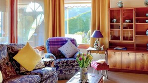 Una sala de estar acogedora con un sofá estampado, una mesita con un jarrón de flores y un aparador de madera con puertas de cristal.