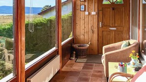 Una habitación acogedora con puerta de madera, cesta de mimbre, sillón mullido y una mesa con un jarrón de flores.