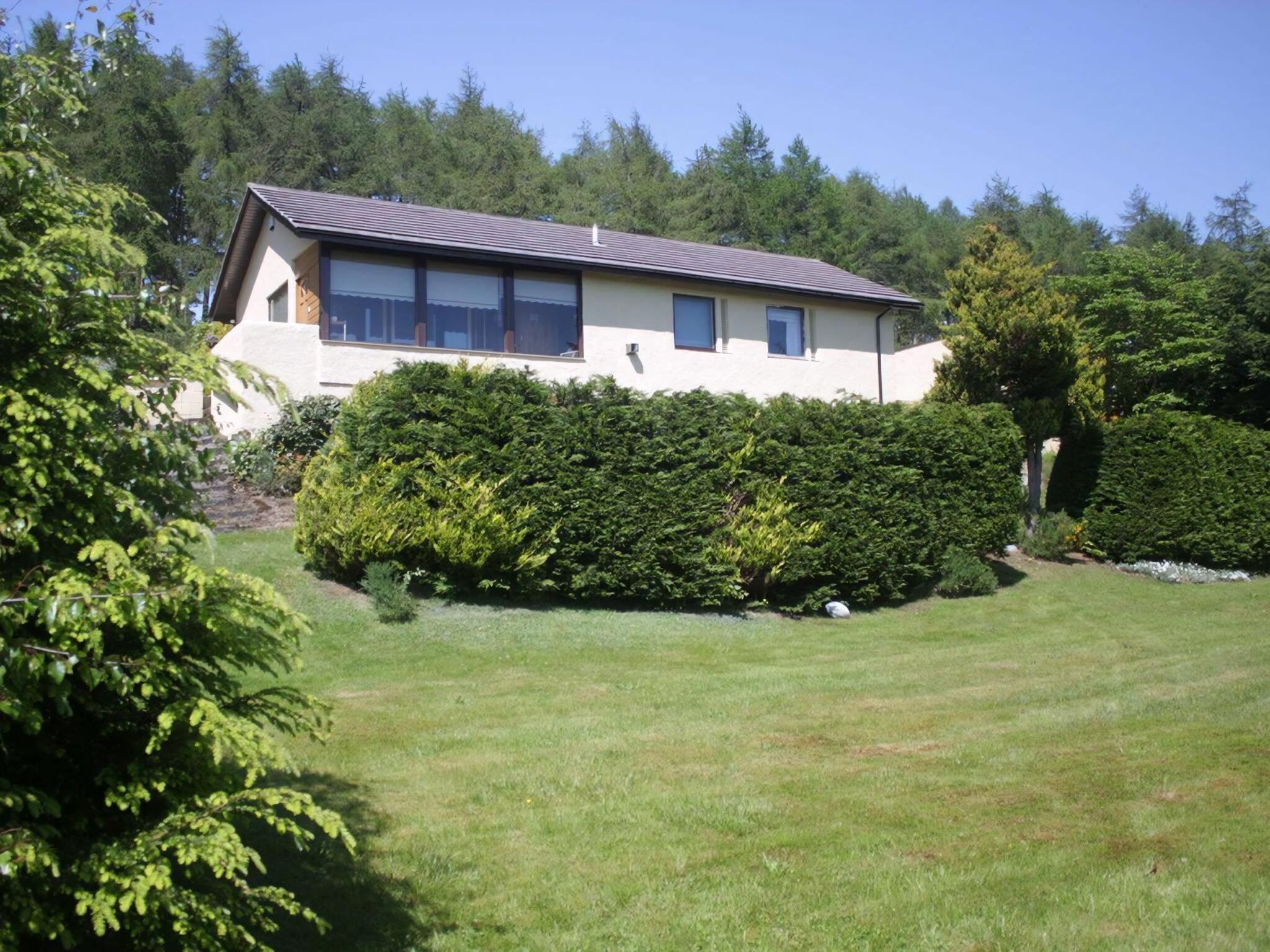 A two-story house with a sloped roof, surrounded by well-maintained hedges and a grassy lawn.