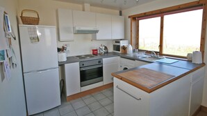 A kitchen with white cabinets, a refrigerator, an oven, a sink, and a window with a view. - 2 bedroom accommodation in North Keiss, Caithness (North Keiss, Caithness)