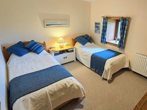 Two single beds with matching headboards, a bedside table with a lamp, a small window with curtains, and a radiator.