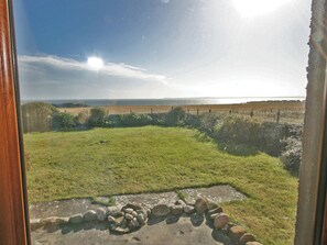 A view through a window with a stone wall, a grassy field, and a distant body of water. - 2 bedroom accommodation in North Keiss, Caithness (North Keiss, Caithness)