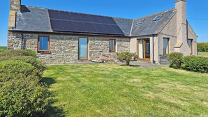 A stone house with a sloped roof, solar panels, and a small garden. - 2 bedroom accommodation in North Keiss, Caithness (North Keiss, Caithness)