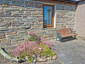 A stone building with a wooden bench and flower beds in front. - 2 bedroom accommodation in North Keiss, Caithness (North Keiss, Caithness)
