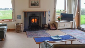 A cozy living room with a fireplace, a television, and a view of the outdoors. - 2 bedroom accommodation in North Keiss, Caithness (North Keiss, Caithness)