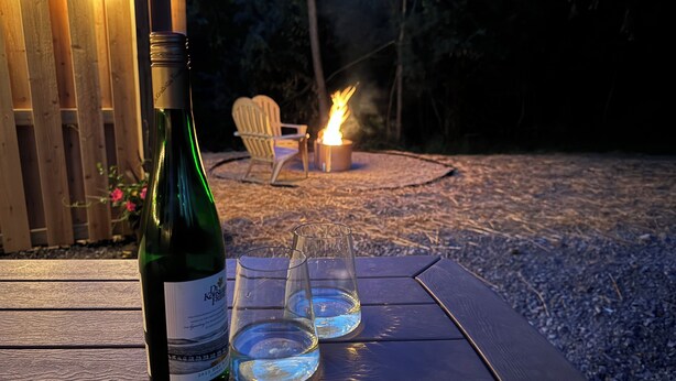 Una botella de vino y dos copas sobre una mesa de madera al aire libre al atardecer.