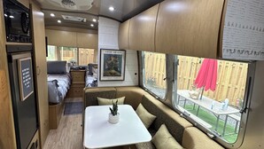 Interior compacto de una caravana con kitchenette, comedor y zona de estar con vista al patio trasero.