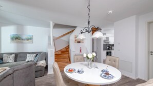 A modern living room with a grey sofa, a round dining table with chairs, and a staircase leading to an upper level. - Awesome home in Olpenitz with sauna (Olpenitz)