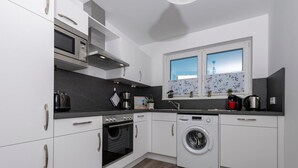 A modern kitchen with white cabinets, a built-in oven, a washing machine, and a window with a view of the sky. - Awesome home in Olpenitz with sauna (Olpenitz)