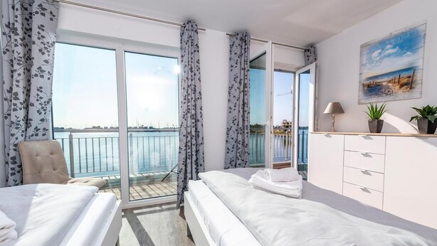 A hotel room with two beds, a balcony with a view of the sea, a painting on the wall, and a small plant on the dresser. - Awesome home in Olpenitz with sauna (Olpenitz)