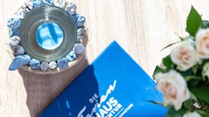 A blue brochure titled "Die Feen Haus Agentur" next to a candle holder with a blue candle. - Awesome home in Olpenitz with sauna (Olpenitz)