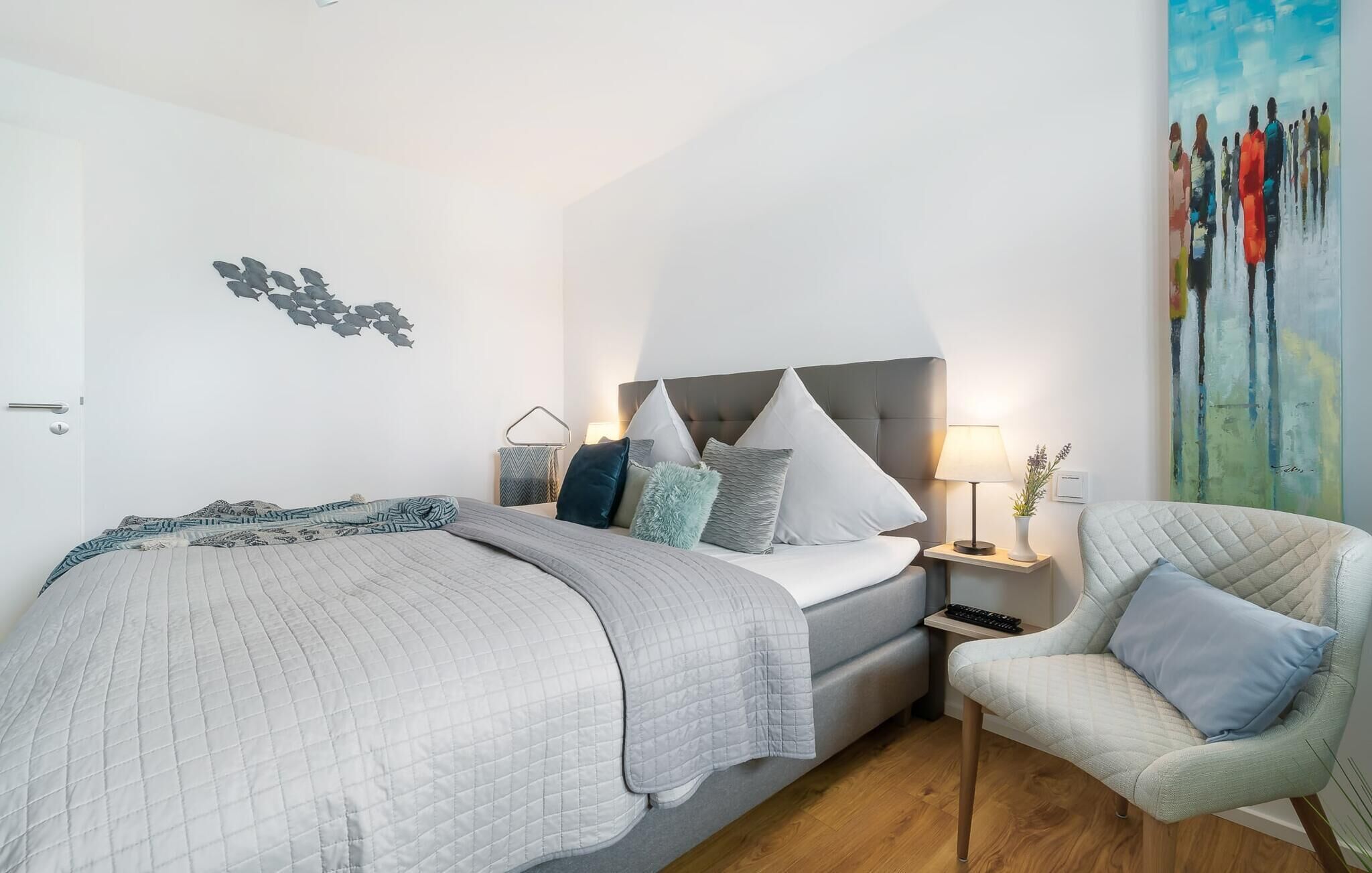 A modern bedroom with a bed, a chair, a nightstand, and a painting on the wall.