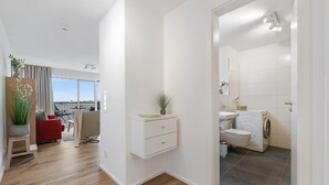 A modern apartment with a wooden floor, a balcony with a view, a small dining area, and a compact bathroom with a washing machine.