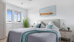 A bedroom with a large bed, a nightstand, a window with a view, and a painting on the wall. - Nice apartment in Olpenitz with WiFi (Olpenitz)