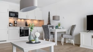 A modern kitchen with white cabinets, a Bosch microwave, and a coffee maker. There is a dining area with a white table, grey chairs, and a vase with flowers. - Nice apartment in Olpenitz with WiFi (Olpenitz)