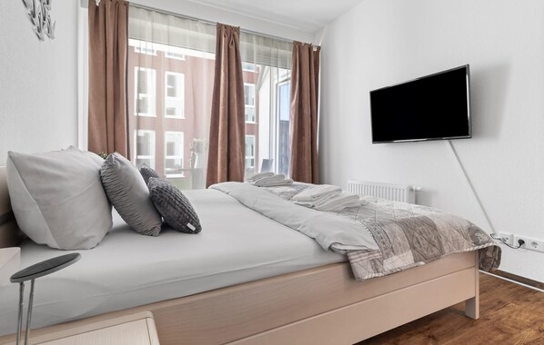 A modern hotel room with a bed, a TV, and a view of a building through the window. - Awesome apartment in Olpenitz with WiFi (Olpenitz)