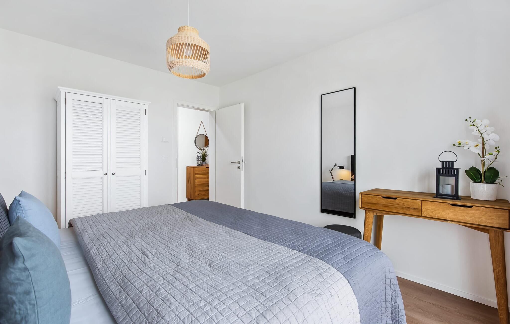 Un dormitorio con cama, un escritorio de madera, un espejo y una lámpara colgante.