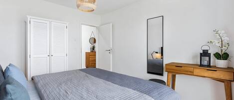 Un dormitorio con cama, un escritorio de madera, un espejo y una lámpara colgante.