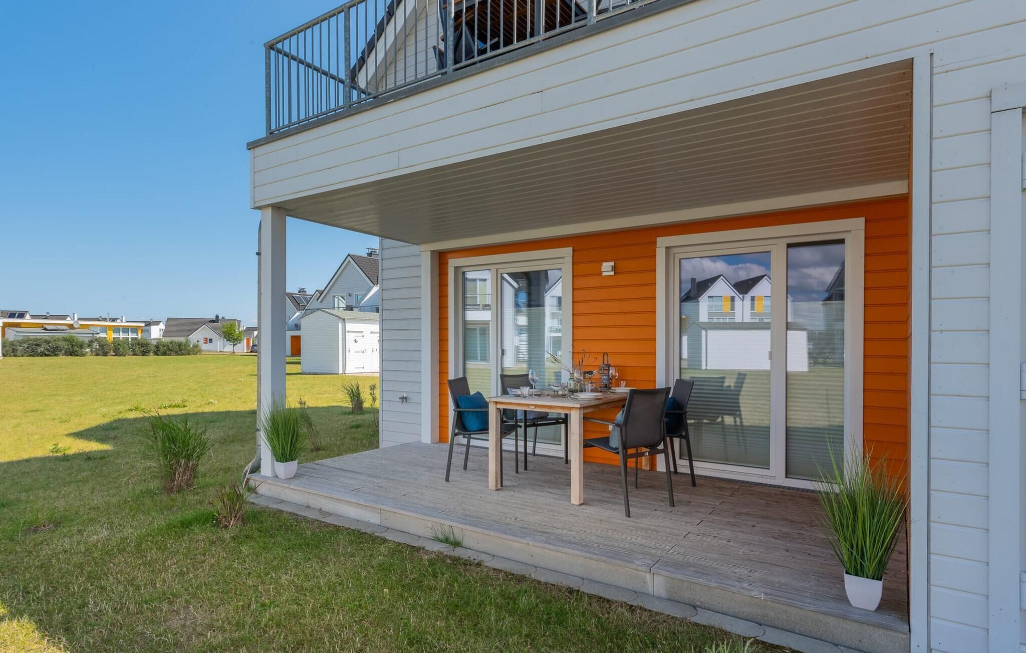 Een tweelaags huis met een overdekte veranda, een eettafel met stoelen en een kleine tuin.