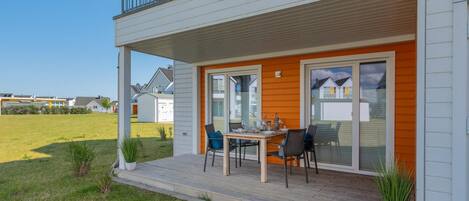 Een tweelaags huis met een overdekte veranda, een eettafel met stoelen en een kleine tuin.