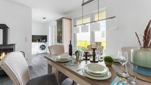 A modern dining area with a wooden table set for four, a fireplace, and a view of the outdoors. - Beach front apartment in Olpenitz (Olpenitz)