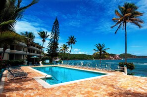 A pool area with lounge chairs and palm trees, overlooking the ocean.