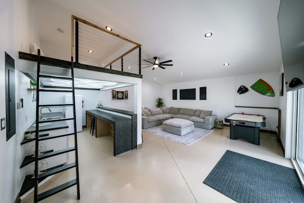 A modern interior with a loft bedroom, a kitchen area, a living room with a sofa, and a dining table.