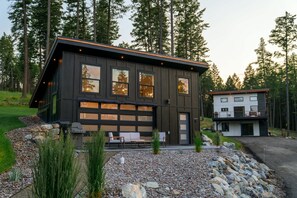 A modern two-story house with a large garage, outdoor seating area, and a well-maintained garden. - Flathead Lake View: Luxe Estate w/ Pool & Hot Tub (Lakeside)