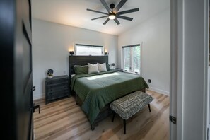 A bedroom with a bed, a dresser, a bench, a ceiling fan, and a window. - Flathead Lake View: Luxe Estate w/ Pool & Hot Tub (Lakeside)